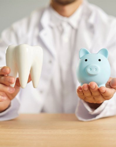 A dentist holding a piggy bank and a healthy white tooth model in his hands.