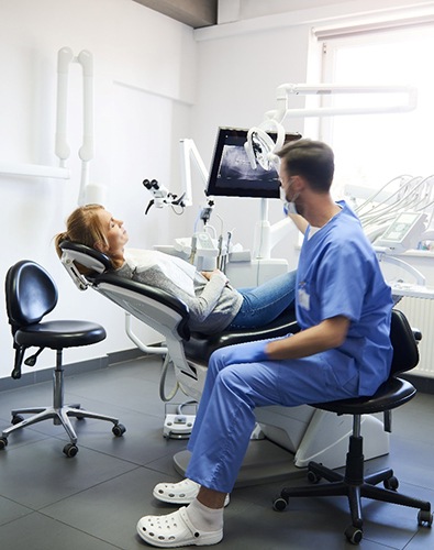 A woman lying back listening to her dentist while the assistant moves around the room to prepare for dental crown placement