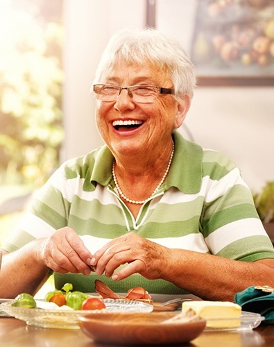 Woman at dining table laughing with dentures in Denton