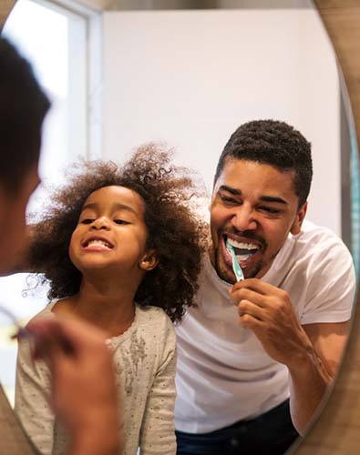 Father and daughter brushing teeth to prevent dental emergencies
