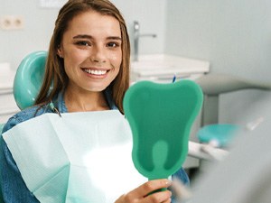 Female patient with handheld mirror after receiving dental implants in Denton, TX