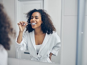 A woman brushing her teeth in front of a bathroom mirror