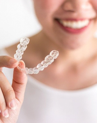person smiling and holding an aligner for Invisalign in Denton, TX