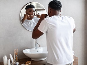 Man smiling while flossing teeth in bathroom
