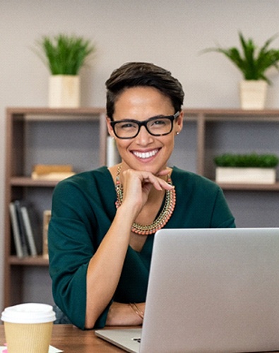 A middle-aged woman seated at a laptop with her coffee and showing off her smile