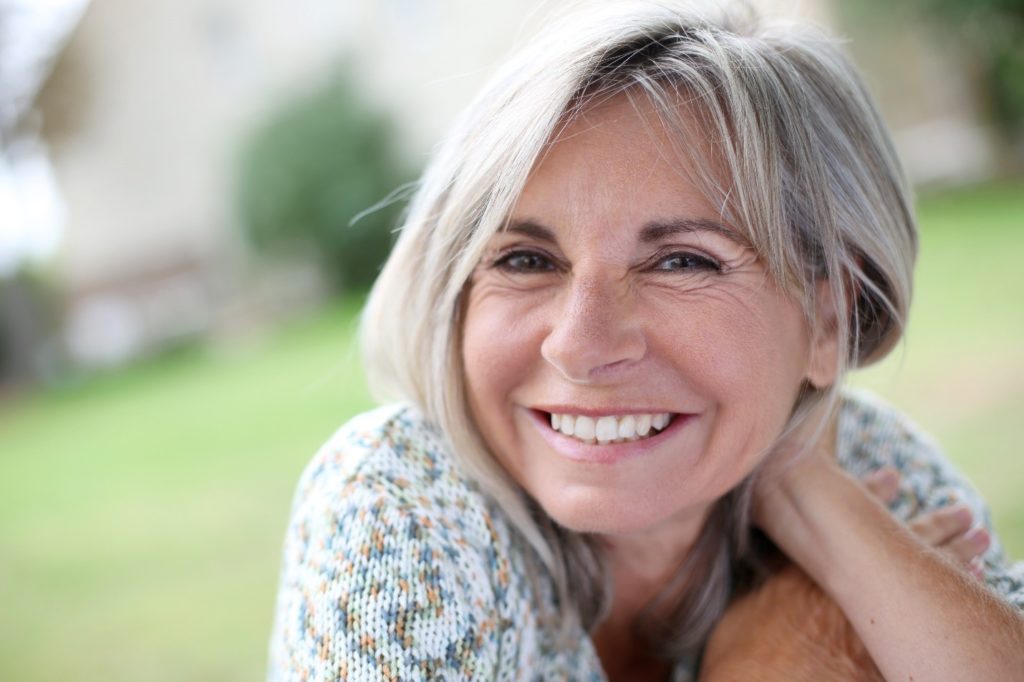 Older woman smiling after receiving dental implants.