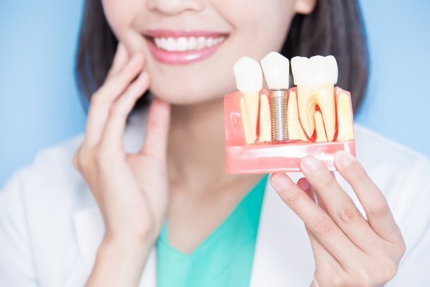 dentist holding dental implant model and touching cheek