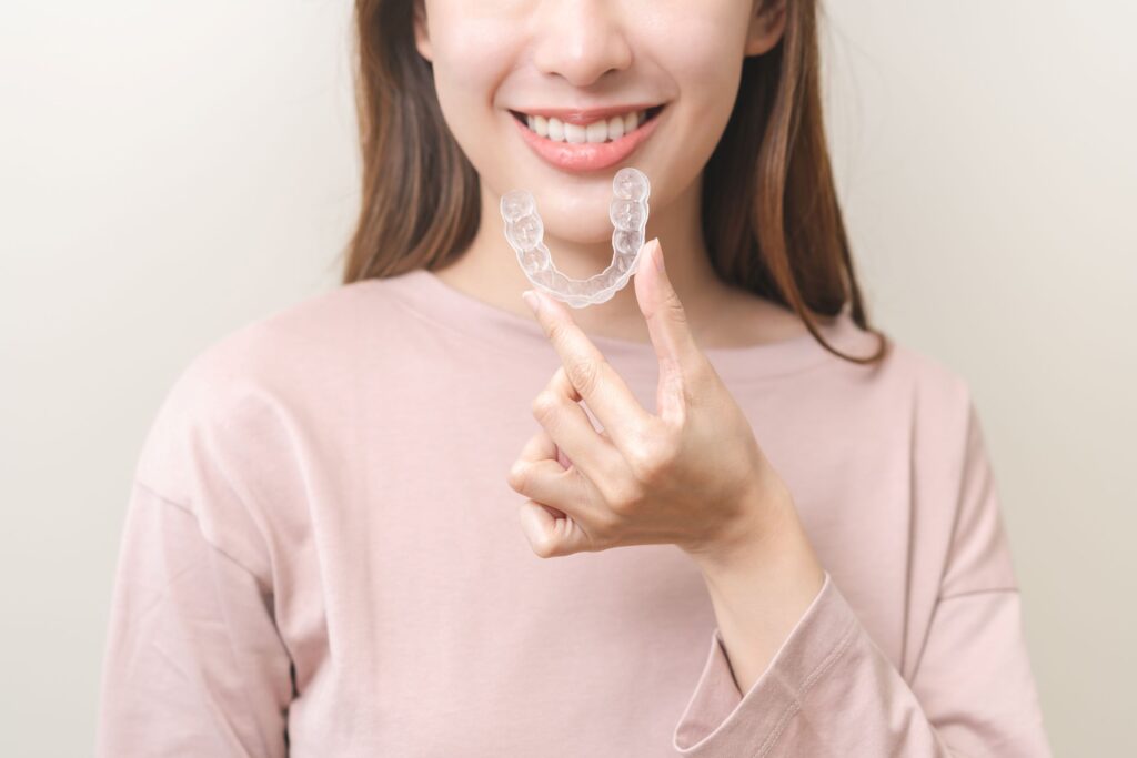 Nose-to-chest view of woman holding clear aligner in front of mouth